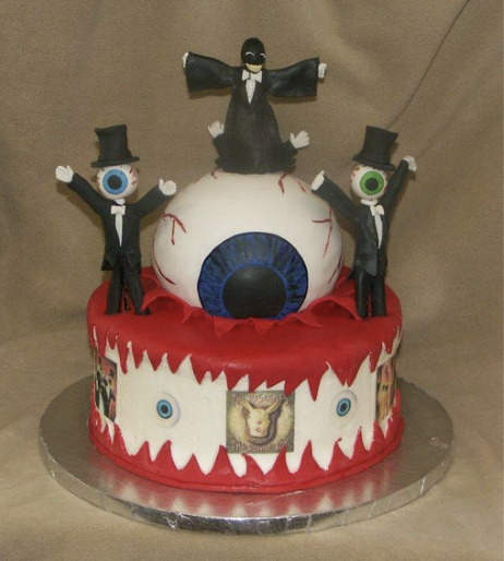 A wormwood themed cake featuring the eyeballs and Mr. Skull, who is dressed in a black robe. Mr. Skull is standing on a large eyeball and the lower half of the cake is decorated with images of 2000s Residents albums.